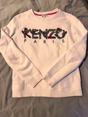 Vit sweatshirt från Kenzo Paris - Vit sweatshirt med broderad Kenzo Paris-logga i svart och röda detaljer. Rund halsringning och långa ärmar. Perfekt för en trendig och avslappnad look.                                                    Skriv för fler bilder och info! Priset går alltid att sänka!🌸 Kolla in profilen för fler saker och lägger upp lite hela tiden! Hör av er om ni söker något!🌸 Skickar inom 1-3 dagar!🌸 