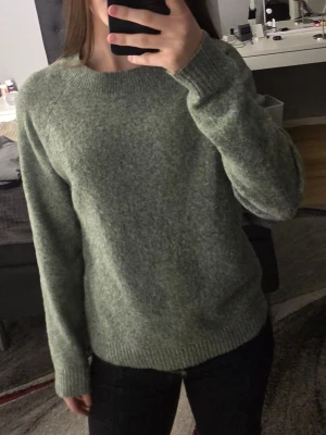 Gråmelerad stickad tröja VERA MODA - Mysig gråmelerad stickad tröja från VERA MODA med rund halsringning och ribbade muddar vid ärmslut och nederkant. Perfekt för kyliga dagar och enkel att matcha med olika outfits. Materialet känns mjukt och behagligt mot huden.