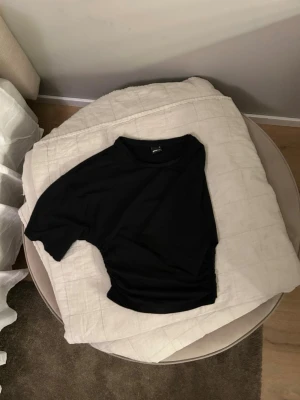 Svart croppad topp med rynkade sidor - Snygg svart croppad topp från Ginatricot med rynkade detaljer på sidorna. Toppen har korta ärmar och en klassisk rund halsringning.  Använd 2 gånger