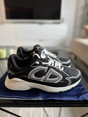 B30 sneakers DIOR - Säljer ett par Dior B30 sneakers i svart/vit färg. Skorna är i storlek 43 och är helt oanvända, i nyskick. Originalsnören medföljer. Observera att varken box eller dustbag ingår.