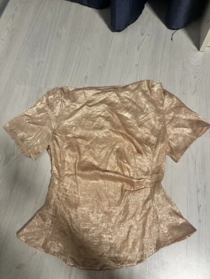 Champagnefärgad glansig blus Shein - Snygg champagnefärgad blus med glansig finish och korta ärmar. Figurnära passform och lätt utsvängd nertill. Perfekt för dig som vill sticka ut med en elegant topp.