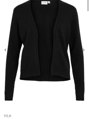 Svart öppen kofta från Vila - Stilren svart öppen kofta från Vila med lång ärm och ribbade muddar. Koftan har en enkel, rak passform och är perfekt att slänga över en t-shirt eller topp. Tillverkad i mjukt stickat material som känns skönt mot huden.