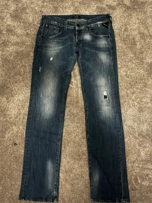 Replay jeans i mörkblå tvätt, strl 31/34 - Snygga Replay jeans i mörkblå tvätt med slitningar och distressed detaljer på både fram- och baksida. Klassisk femficksmodell med raka ben och normal passform. Materialet är robust jeans och byxorna har en cool, lite sliten look som passar till streetwear. Storlek: midja 31, längd 34. Pris kan diskuteras 