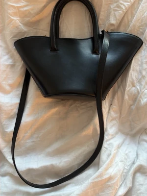 Little liffner Open tulip micro - Säljer en så snygg svart handväska i skinn med unik design från märket little liffner. Modellen heter Open tulip micro och är i bra skick. Den har både handtag och axelrem. Är i kalvskinn och får därför små repor lätt, men inget man märker så tydligt. Skriv gärna vid fler frågor. 💗