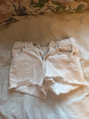 Vita jeansshorts från Zara - Snygga vita jeansshorts från Zara med råa kanter och klassisk femficksdesign. Shortsen har knapp- och dragkedjestängning samt slitna detaljer för en trendig look. Perfekta för varma dagar och enkel att matcha med allt.