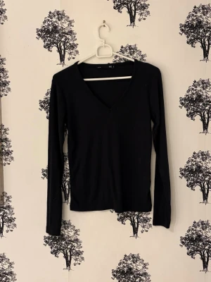 Svart ribbad långärmad topp - En svart långärmad topp med v-ringning och ribbad struktur. Toppen har en slim passform och är perfekt att styla med jeans eller kjol. Enkel och stilren design som funkar till många olika looks.