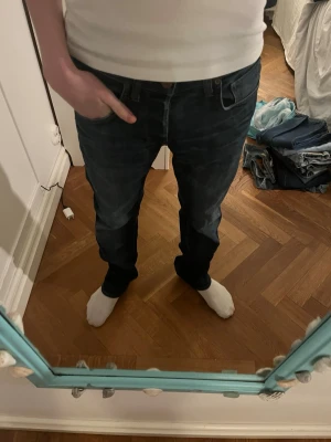 Mörkblå raka jeans herr - Säljer ett par mörkblå jeans med rak passform och klassiska fem fickor. Jeansen har en enkel design med subtila sömmar och är perfekta för en avslappnad stil. Materialet är denim i bomull och de har normal midja.