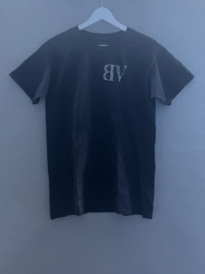 Rhinestone T-shirt - Snygg svart t-shirt från BVALDI med korta ärmar. På bröstet står det 'BV' och på ryggen 'BVALDI', båda i glittriga strasstenar. Perfekt för dig som gillar stilrena plagg med lite extra bling. Klassisk passform och mjukt material.