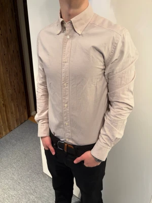 These glory Days Skjorta Beige  - Den är i fint skick och i storlek L. Klassisk beige skjorta med lång ärm och knappar framtill. Skjortan har button down-krage och är tillverkad i ett mjukt bomullstyg. Perfekt för en clean och stilren look.