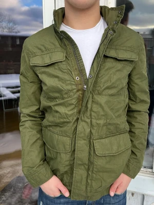 Olivgrön fieldjacket - Otroligt snygg fieldjacket i olivgrön perfekt för våren som kommer. Den är storlek S men passar mer M enligt mig, väldigt bra skick och bara att höra av dig vid frågor!🙌🙌🤩