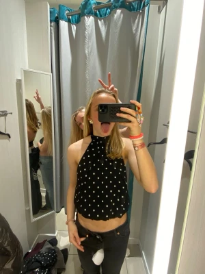 Snygg halterneck - Trendig svart halterneck topp med vita prickar. Perfekt för dig som vill sticka ut med en cool topp. Toppen är ärmlös och har en snygg, öppen rygg. Använd vid endast ett tillfälle.