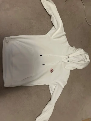 Casablanca hoodie  - Snygg vit hoodie med huva och dragsko, samt stor magficka framtill. Liten röd logga på bröstet ger en clean look. Perfekt för dig som gillar enkel och stilren streetwear. Mjuk bomullskänsla och relaxed fit.