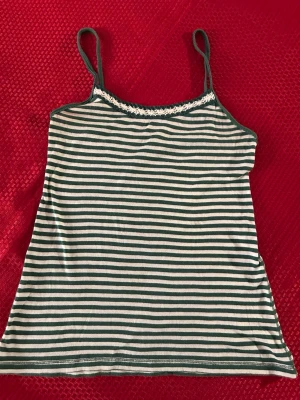 Randig linnetopp med spetsdetalj - Snygg randig linnetopp med gröna och vita ränder samt smala axelband. Toppen har en söt spetsdetalj längs halsringningen och är perfekt för varma dagar.