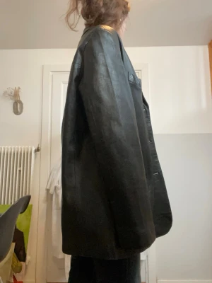 Oversized svart skinnjacka - Snygg oversized svart skinnjacka med klassisk krage och knäppning framtill. Jackan har raka ärmar och två fickor framtill. Perfekt för en cool och avslappnad stil. Passar till jeans eller byxor för en trendig look.
