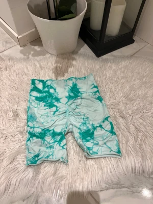 Turkosa tie-dye gym shorts  - Säljer ett par trendiga gym shorts i turkos och vit tie-dye. De är stretchiga och har en bekväm passform som slutar ovanför knäna. Perfekta för en avslappnad och sportig look. Materialet känns mjukt och följsamt.