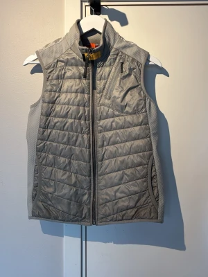 Parajumpers väst - Snygg ljusgrå dunväst med quiltat mönster och hög krage. Västen har hel dragkedja framtill, bröstficka med dragkedja och sidofickor. Materialet är en mix av dun och syntet, med stretchpaneler på sidorna för extra komfort. Perfekt för lager-på-lager och streetwear. Riktigt fet väst enligt mig och i jätte bra skick inga defekter. Perfekt för våren🌷🌼