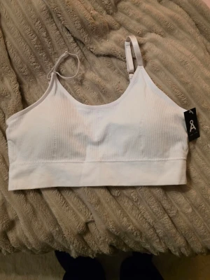 Vit ribbad bh från Åhléns L/XL - Säljer en vit ribbad bh från Åhléns i storlek L/XL. Bh:n har smala axelband och bred resår under bysten för extra komfort. Tillverkad i mjukt och stretchigt material som sitter skönt mot kroppen. Perfekt för dig som gillar enkel och stilren design.