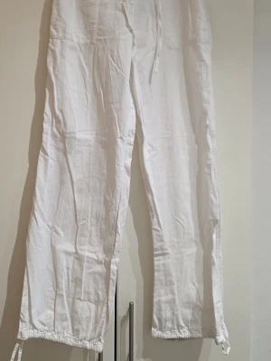 Vita linnebyxor med dragsko - Snygga vita linnebyxor med avslappnad passform och dragsko i midjan samt vid bensluten. Byxorna är tillverkade i ett lätt och luftigt linnematerial, perfekta för varma dagar. Klassisk design utan synligt märke.