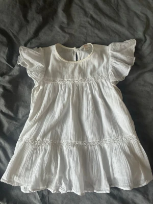 Vit volangtopp  - Söt vit blus med volangdetaljer och korta ärmar. Tillverkad i luftig bomull med rund halsringning och lätt rynkade sömmar för en flowy känsla. Perfekt för varma sommardagar