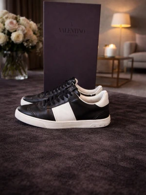 Valentino Garavani svartvita sneakers - Snygga sneakers från Valentino Garavani i svart och vitt läder. Klassisk låg modell med svart ovandel, vit sidopanel och vit sula. Skorna har svarta skosnören och diskret logga på plösen. Perfekta för dig som gillar stilrena och exklusiva sneakers.