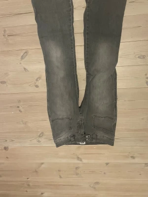 Grå bootcut jeans med fickor - Säljer ett par grå bootcut jeans med klassiska fem fickor och knappgylf. Jeansen har en lätt utsvängd passform nedtill och är tillverkade i ett mjukt denimtyg. Perfekta för dig som gillar en avslappnad men ändå trendig look.