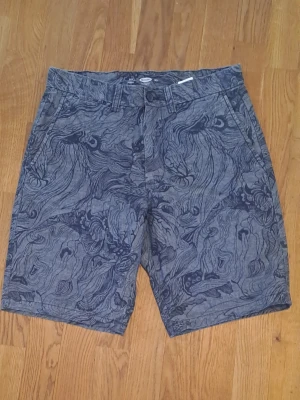 Mönstrade grå/blå shorts från Old Navy - Säljer ett par blå/graå shorts från Old Navy med unikt mönster i mörkare blå toner i 100% bomull. Shortsen har fickor fram och bak och stängs med dragkedja och knapp. 
