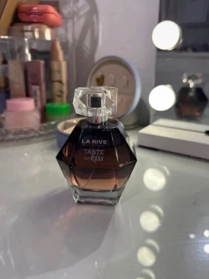 La Rive Taste of Kiss parfym 100ml - La Rive Taste of Kiss är en parfym i en elegant, mörkbrun glasflaska med diamantformad design och transparent lock. Flaskan rymmer 100 ml och har en lyxig känsla som passar perfekt på sminkbordet. Doften är feminin och modern.