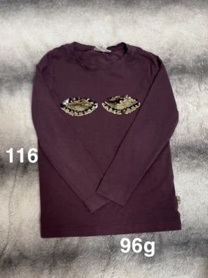 Långärmad vinröd topp med paljetter - Vinröd långärmad topp med två ögon i guld- och silverpaljetter på bröstet. Rund halsringning och normal passform. Perfekt för dig som vill sticka ut lite extra.🌸 Fint använt skick. Storlek 116