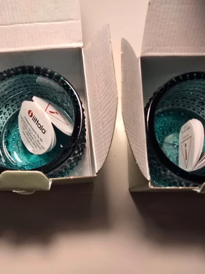 Iittala Kastehelmi ljuslyktor - Två stycken Iittala Kastehelmi ljuslyktor i blått glas. Aldrig använda. Ljuslyktorna har en rund form och är dekorerade med små glasbubblor runt om, vilket ger ett snyggt och klassiskt utseende. Perfekta för värmeljus och levereras i originalkartong.