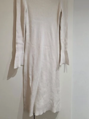 Vit ribbad långärmad klänning - Snygg vit ribbad klänning med lång ärm och rak passform. Klänningen har en enkel och stilren design med diskret struktur i materialet. Perfekt för dig som gillar minimalistisk stil.