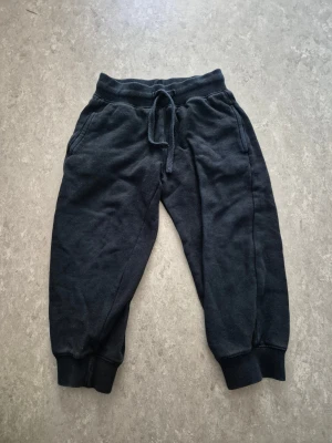 Mjukisbyxor - Mörka svarta mjukisbyxor från BASIC U i storlek 98/104. Byxorna har resår och snörning i midjan, ribbade muddar vid bensluten och två sidofickor. Perfekta för chill dagar eller träning. Mjukt och bekvämt material. Har hål.