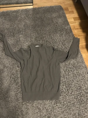 Grå stickad tröja från H&M - En enkel och stilren grå stickad tröja från H&M. Tröjan har rund halsringning, ribb fold vid ärmslut och nederkant samt lång ärm. Perfekt till jeans eller över bara en t-shirt för en clean look.