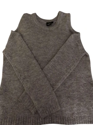 Grå stickad tröja från LMTD ( Utan axlar - Mysig grå stickad tröja från LMTD med rund halsringning och långa ärmar. Tröjan har ribbade muddar vid ärmslut och nederkant, perfekt för kyliga dagar. Enkel och stilren design som passar till det mesta.