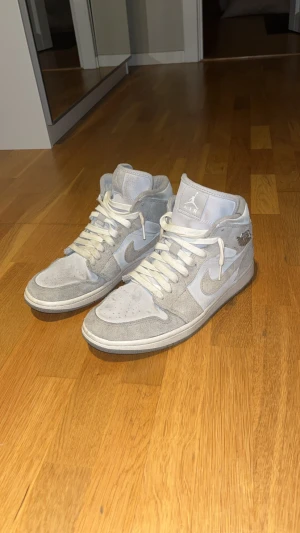 Nike Air Jordan 1 Mid grå mocka - Nike Air Jordan 1 Mid sneakers i ljusgrå färg med snyggt mocka-överdrag.  ”Air jordan” spänne av metall på sidan av båda skorna. Nypris ca 1500. Bra skick med några skavanker men inget som inte borde gå att tvättas bort. Hör gärna av er vid frågor eller funderingar! 