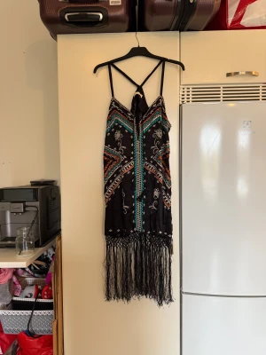 Odd Molly boho kortklänning med fransar - Supersnygg svart kortklänning från Odd Molly med boho-vibe, broderade detaljer i turkos, orange och vitt samt coola fransar längst ner. Klänningen har smala axelband som korsas i ryggen och snörning framtill. Perfekt för dig som gillar unika mönster och festivalstil! Från märket Odd Molly. Storlek 3 som enligt deras storleksguide motsvarar en L. Mycket fint skick, jag hittar inga synliga anmärkningar eller defekter. 