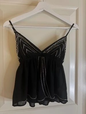 Svart glittrig topp - Svart linnetopp från Subdued i storlek S med tunna justerbara axelband och glittriga silverdetaljer framtill. Köpte i somras men kommer aldrig till användning så skicket är nästan som nytt. inga defekter eller hål. Kostar originellt 460 