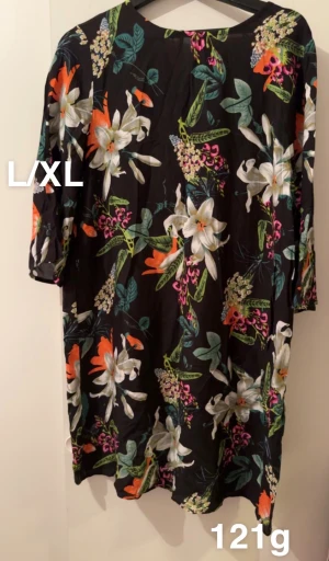 Blommig svart klänning L/XL - Svart klänning med färgglatt blommönster i vitt, orange, grönt och rosa. Modellen är rak och har trekvartsärmar. Perfekt för dig som gillar en färgstark och bekväm stil. 🌸 Fint använt skick. Storlek L/XL