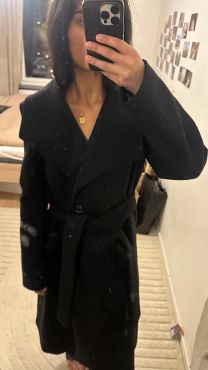 Svart ull kappa med bälte från Mango - Säljer en svart kappa från mango och den är helfodrad för extra värme. Perfekt för kalla dagar. Även ullblanding. Nypris 2200 och använd två gånger