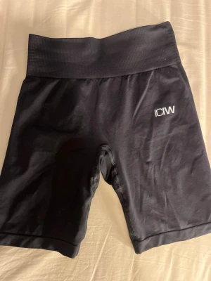 Svarta högmidjade träningsshorts ICANIWILL - Svarta, tighta och högmidjade träningsshorts från ICANIWILL. Snygg ribbad midja och diskret logga framtill. Materialet är stretchigt, vilket gör dem perfekta för gymmet eller löpning. Sitter skönt och formar kroppen.