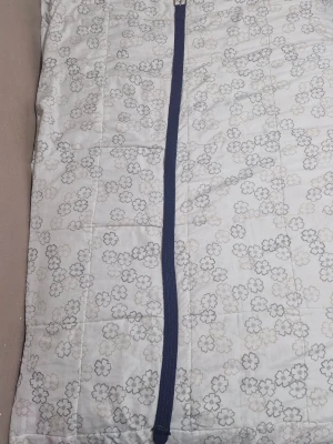 Jack n Jones bälte - Quiltad dunväst i vit med blommigt mönster i grå toner. Västen har en blå bälte med silverfärgat spänne som detalj. Perfekt för dig som gillar en chill och snygg look. Materialet är mjukt och lätt, och västen har en rak passform.