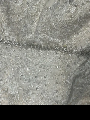 Vit långkjol med spets och paljetter - Vit långkjol med lyxig spets och broderade blommor, dekorerad med paljetter och pärlor som ger extra glans. Kjolen har en elegant och voluminös form, perfekt för speciella tillfällen. Materialet är troligtvis polyester eller siden med spetsdetaljer.