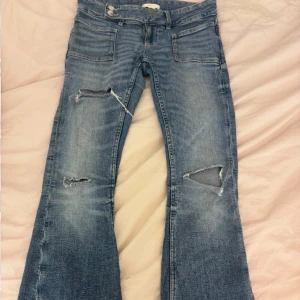 Blå bootcut jeans med slitningar - Snygga blå jeans med bootcut passform och slitna detaljer på benen. Jeansen har klassiska fickor fram och bak, samt bälteshällor. Materialet är jeans med en tvättad look och tydliga slitningar för en cool vibe. Dem är från Gina Tricot 14+.