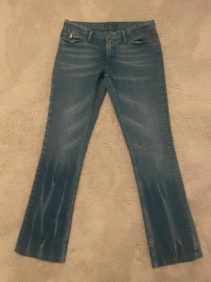 Blå bootcut jeans från Ralph Lauren - Snygga blå jeans från Ralph Lauren i klassisk bootcut-modell. Jeansen har en lätt tvättad look med slitningar och raka ben som blir vidare nertill. Tillverkade i jeansmaterial med fem fickor och knappgylf. Perfekta för en avslappnad och trendig stil.  Köpte men passade inte gick inte lämna tillbaka 