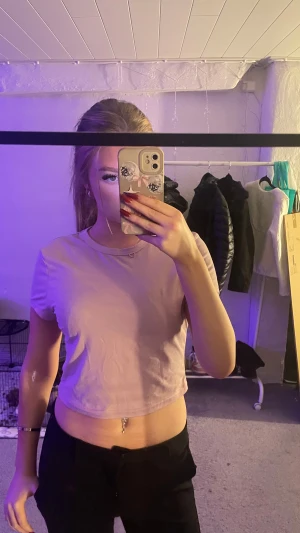 Ljusrosa croppad t-shirt topp - Säljer en ljusrosa croppad t-shirt topp med rund hals och korta ärmar. Toppen är enkel och stilren, perfekt att matcha med jeans eller kjol. Materialet känns som mjuk bomull och färgen är soft rosa. Passformen är normal och toppen är ärmlös vid axlarna.