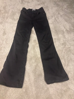 Svarta bootcut jeans från 157, strl 150 - Svarta jeans från 157 i modellen 90's Boot Star, storlek 150. Snygg bootcut passform med klassiska fem fickor och knappar på bakfickorna. Jeansen har en rak midja och är tillverkade i mjukt denimtyg som sitter skönt hela dagen.