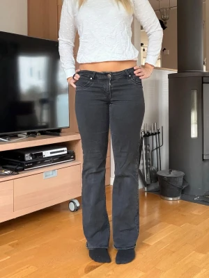 Svarta bootcut jeans Lågmidjade  - Säljer ett par svarta jeans med bootcut-modell och klassisk femficksdesign. Jeansen har lågmidja och är i stretchigt denimtyg som sitter snyggt över höfterna och låren. Perfekta för dig som gillar en tidlös look med lite utsvängda ben.