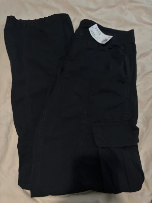 Svarta cargopants  - Svarta cargopants från h&m i storlek 36. Byxorna har elastisk midja, sidofickor och klassiska cargofickor med lock på benen. Materialet är bomull och de har en loose passform som ger en chill vibe.