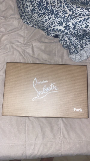 Christian Louboutin svarta sneakers med nitar - Svarta sneakers från Christian Louboutin med ikonisk röd sula och svarta nitar på tån. Skorna har snörning och är tillverkade i skinn. Kommer med originalkartong, dustbag och äkthetskort. Perfekt för dig som vill sticka ut med lyxig streetstyle.