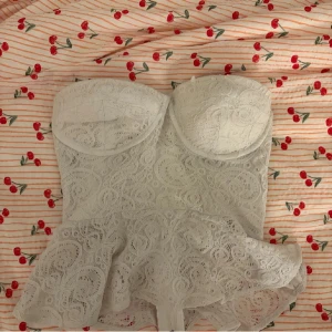 Vit spetskorsett från Bik Bok - Supersöt vit korsett från Bik Bok i storlek S. Toppen är axelbandslös med snygg spets och volang nedtill. Den har en dragkedja i ryggen och formade kupor för extra support. Perfekt för dig som vill ha en feminin och trendig look.