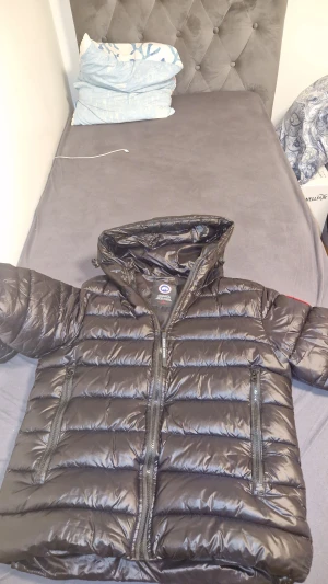 Svart dunjacka från Canada Goose - Säljer en svart dunjacka från Canada Goose med huva och två stora dragkedjefickor framtill. Jackan har quiltad design, reflekterande detaljer på huvan och klassisk Canada Goose-logga på ärmen. Perfekt för kalla dagar och riktigt snygg streetstil.